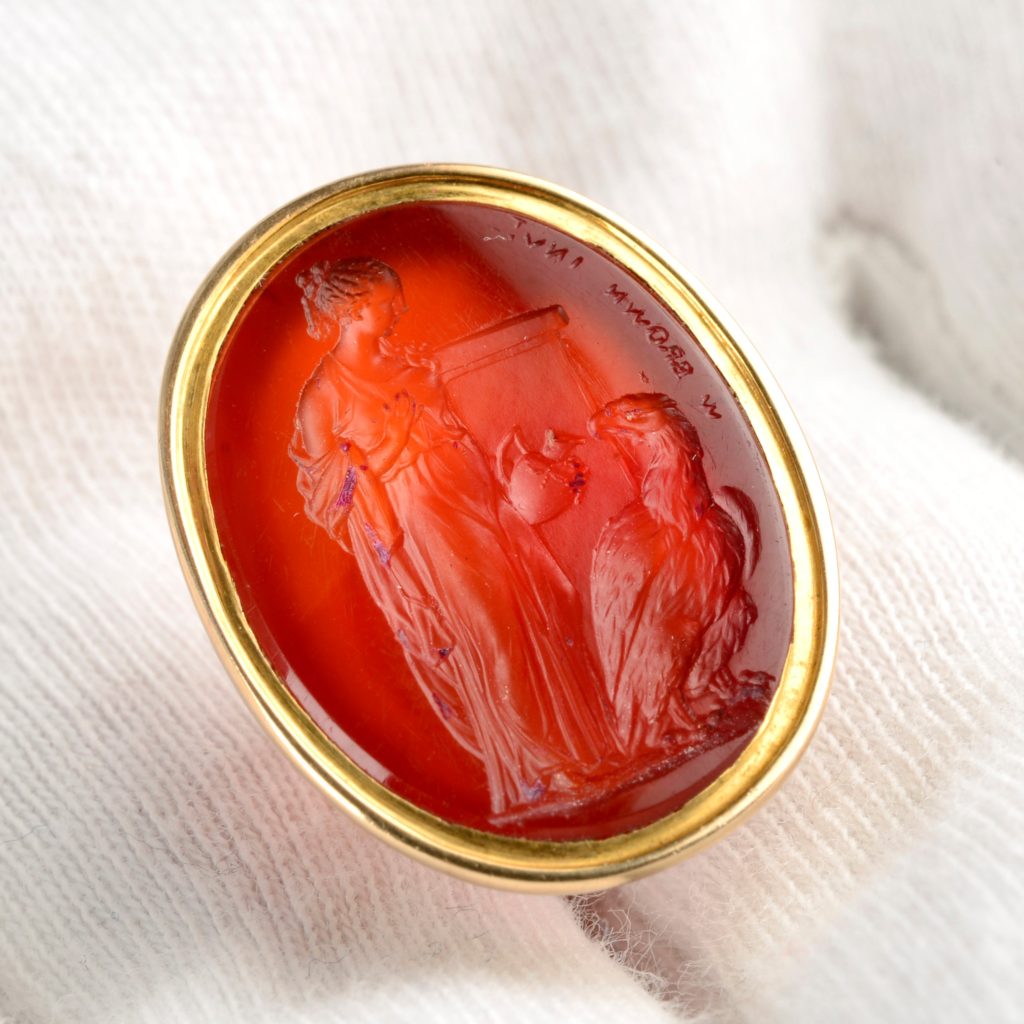 A Late Georgian gold carnelian intaglio of Hebe feeding Zeus as an eagle, by William Brown.